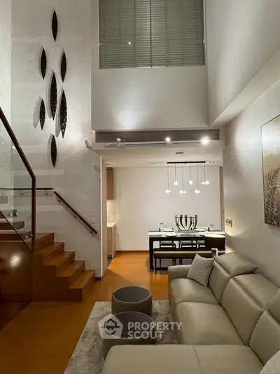 Luxurious modern living room with high ceiling and elegant staircase, perfect for sophisticated urban living.