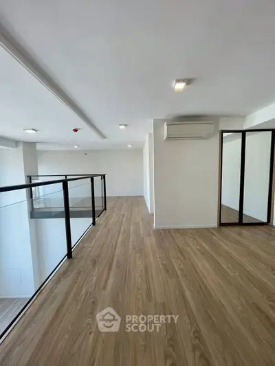 Spacious modern loft with wooden flooring and glass railing, perfect for stylish urban living.