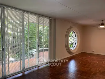 Spacious living room with unique circular window and garden view, perfect for relaxation.