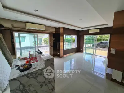 Spacious modern living room with marble accents and large windows offering natural light and garden view.