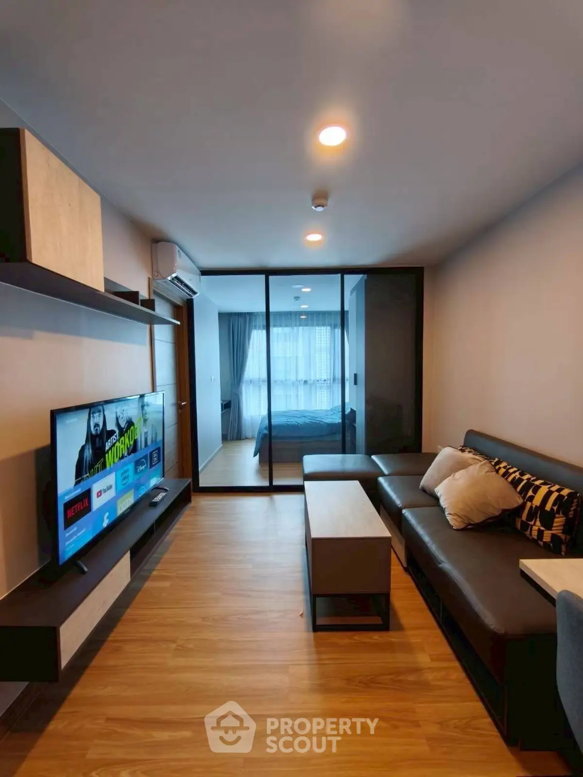 Modern living room with sleek furniture and TV, open view to bedroom
