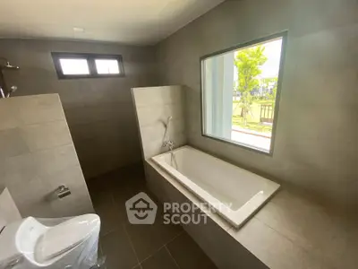 Modern bathroom with large window and built-in bathtub, offering a serene view.