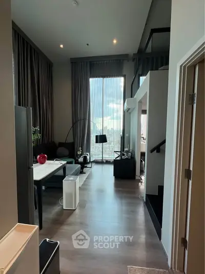 Modern loft-style living room with high ceilings and large windows offering city views.