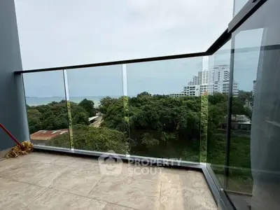 Stunning balcony view with glass railing overlooking lush greenery and distant ocean.