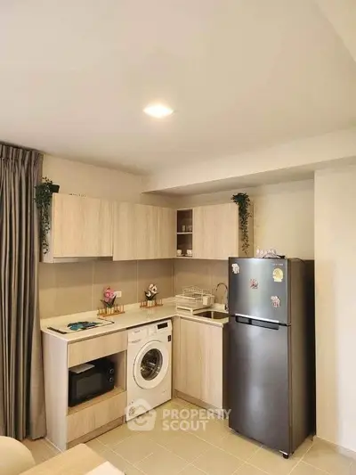 Modern kitchen with washing machine, fridge, and microwave in a cozy apartment setting.