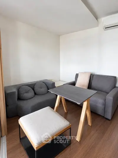 Modern living room with stylish furniture and wooden flooring, featuring a cozy seating area and air conditioning.