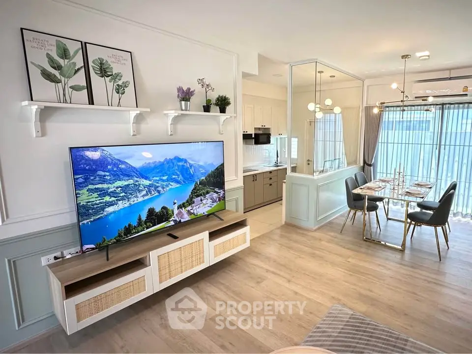 Modern open-plan living room with large TV and dining area, featuring stylish decor and natural light.