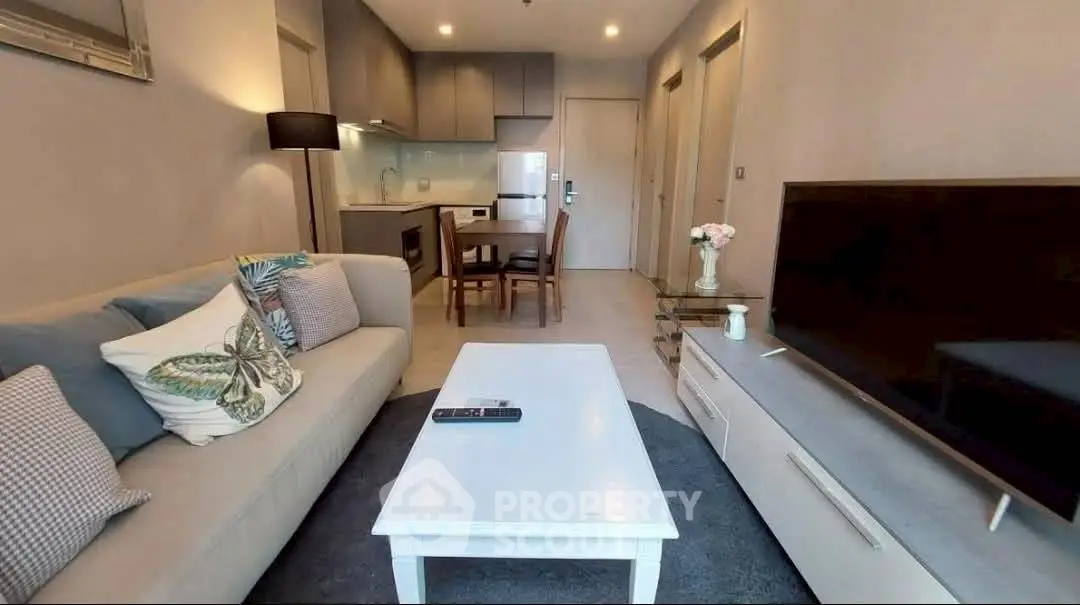 Modern living room with cozy sofa, flat-screen TV, and compact kitchen in open layout apartment.