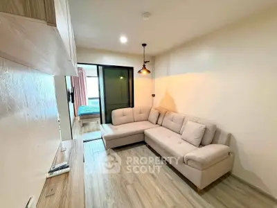Modern living room with cozy beige sectional sofa and wooden flooring, leading to a bedroom.