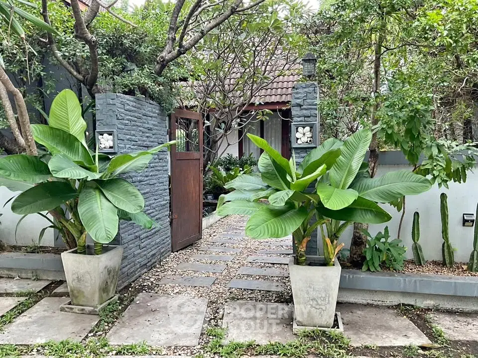 Charming garden entrance with lush greenery and stone pathway leading to a cozy home.