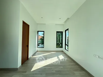 Spacious sunlit room with large windows and wooden door, perfect for modern living.