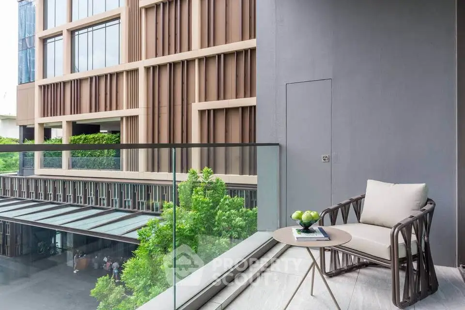 Modern balcony with stylish chair and table overlooking lush greenery and contemporary building facade.