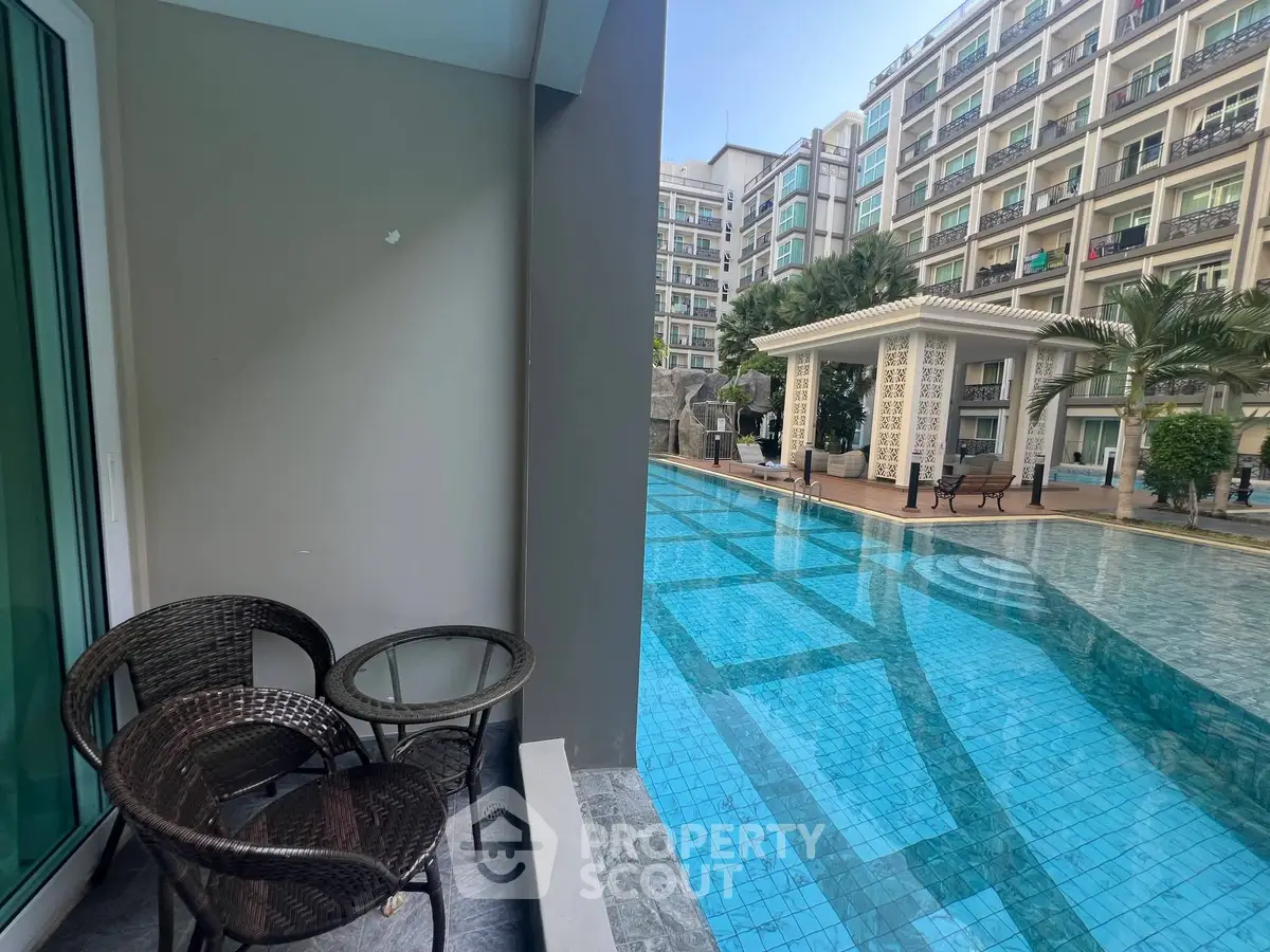 Luxurious poolside view with modern apartment backdrop and cozy balcony seating.