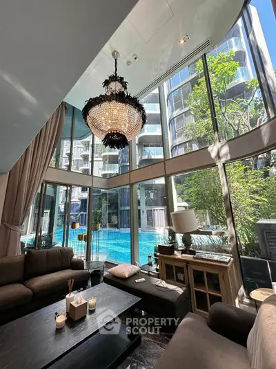 Luxurious living room with floor-to-ceiling windows overlooking a stunning pool view, featuring elegant chandelier.