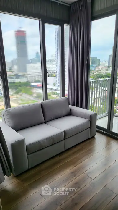 Modern living room with city view and cozy gray sofa in high-rise apartment.