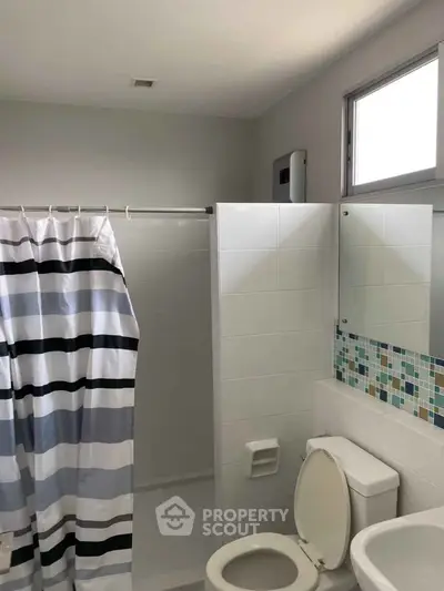 Modern bathroom with shower curtain and tiled walls, featuring a window for natural light.