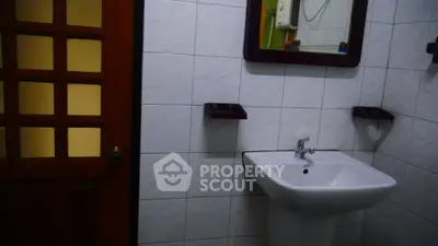 Cozy bathroom with pedestal sink and wooden door, perfect for compact spaces.