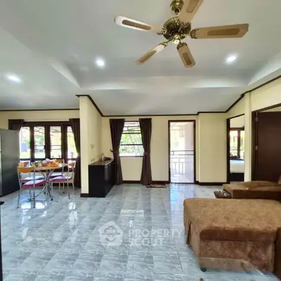 Spacious living room with ceiling fan and dining area, featuring large windows and natural light.