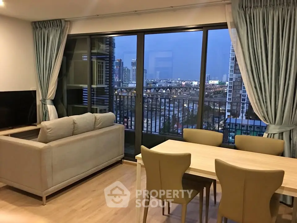 Modern living room with large windows offering stunning city view, featuring elegant furniture and dining area.