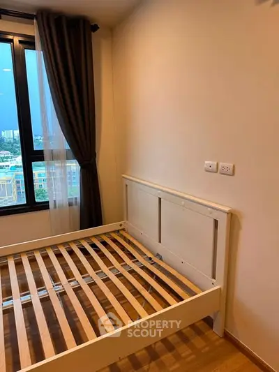 Cozy bedroom with wooden flooring and large window offering city views, perfect for urban living.
