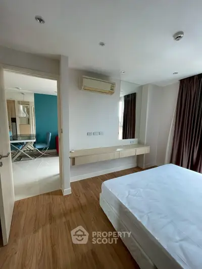 Spacious bedroom with modern decor and wooden flooring, featuring an air conditioner and large window.