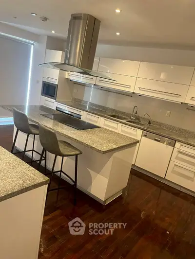 Modern kitchen with sleek white cabinets and granite countertops, featuring an island and built-in appliances.