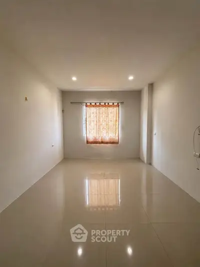 Spacious empty room with tiled flooring and a window with curtains, ideal for customization.