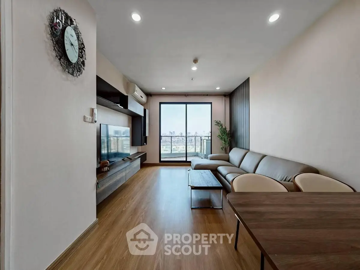 Spacious modern living room with large window and city view, featuring elegant furniture and wooden flooring.