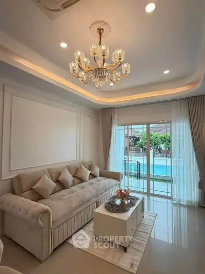 Elegant living room with chandelier, plush sofa, and pool view through sliding glass doors.