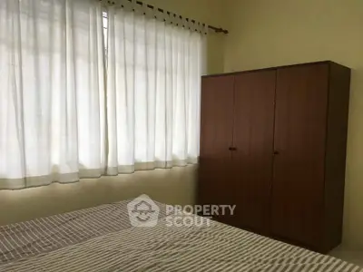 Cozy bedroom with natural light and wooden wardrobe, perfect for relaxation.