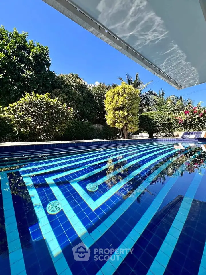 Luxurious outdoor pool with vibrant blue tiles and lush greenery, perfect for relaxation and leisure.