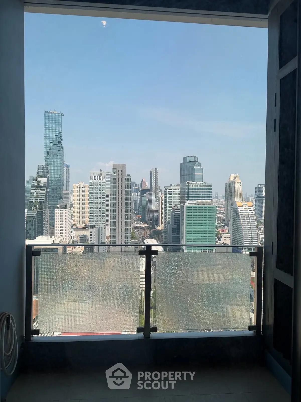 Stunning cityscape view from a high-rise balcony, showcasing modern skyscrapers under a clear blue sky.