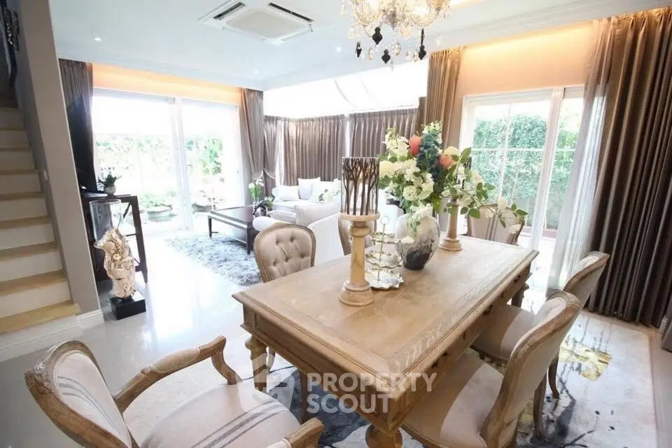 Elegant dining area with natural light and garden view, featuring classic wooden furniture and chandelier.