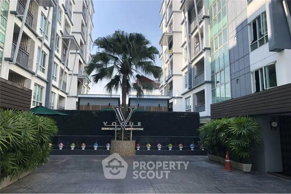 Modern condominium entrance with palm tree and stylish facade, offering urban living in a vibrant community.