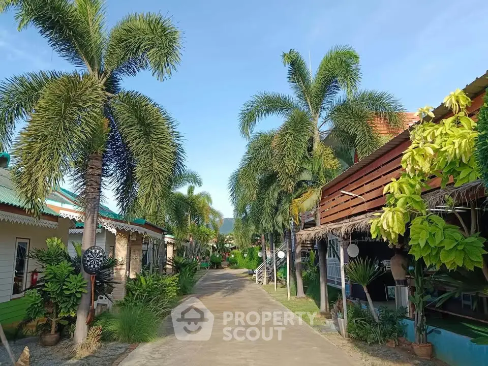 Charming tropical resort with lush palm trees and vibrant cottages under a clear blue sky.