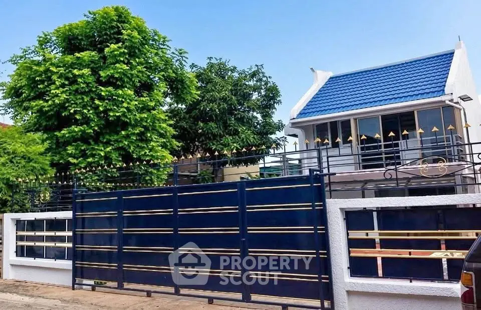 Charming blue-roofed house with modern gate and lush greenery, perfect for serene living.