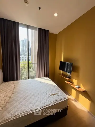 Cozy bedroom with natural light and city view, featuring a wall-mounted TV and modern decor.