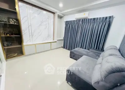 Modern living room with plush gray sofa, marble accent wall, and sleek cabinetry.