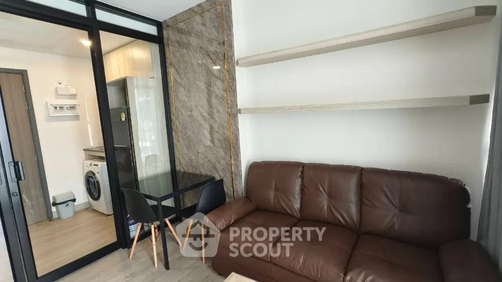 Modern living room with brown leather sofa and glass dining table adjacent to kitchen area.