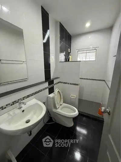 Modern bathroom with sleek black and white tiles, featuring a toilet, sink, and shower area.