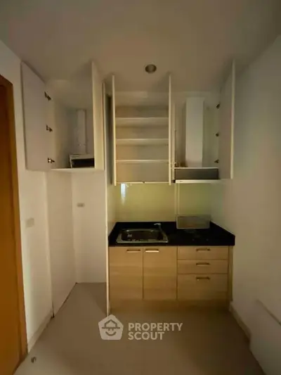 Compact kitchen with open cabinets and black countertop in modern apartment