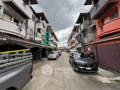 Charming residential street with colorful townhouses and parked cars under a cloudy sky.