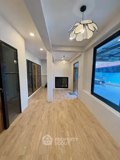 Modern living room with wooden flooring and stylish lighting, featuring large windows and a cozy fireplace.