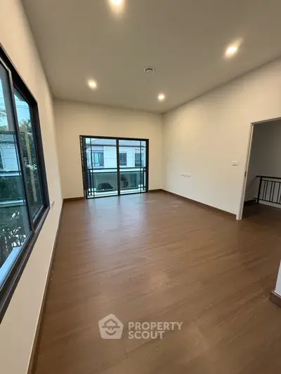 Spacious empty room with wooden flooring and large windows leading to a balcony.