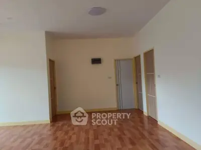 Spacious empty room with wooden flooring and multiple doors, perfect for customization.