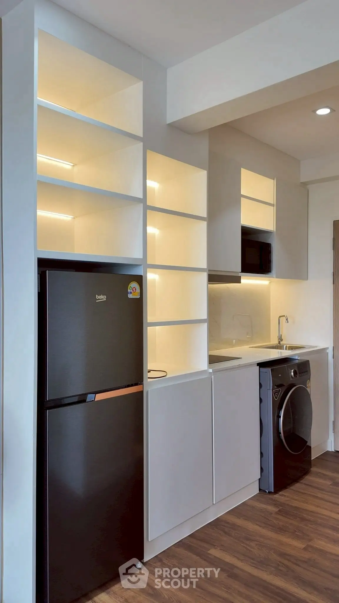 Modern kitchen with sleek appliances and open shelving, featuring a fridge and washing machine.