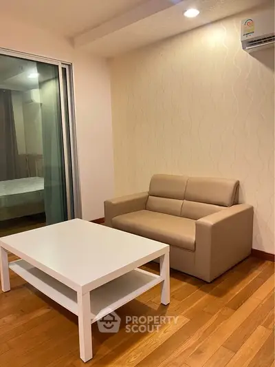Cozy living room with modern sofa and coffee table, featuring wooden flooring and sliding glass door.