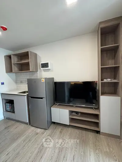 Modern kitchen with fridge, microwave, and stylish cabinetry in compact apartment