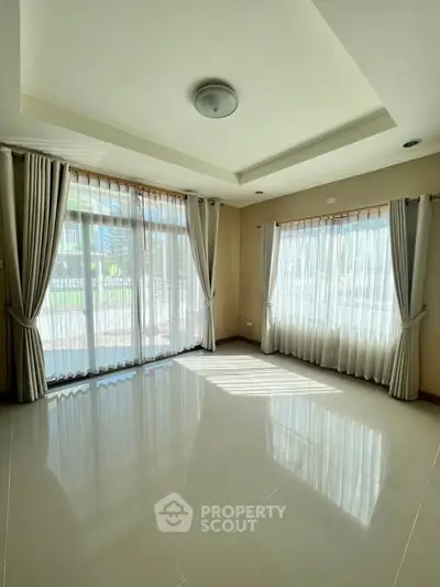 Spacious sunlit room with large windows and elegant curtains, perfect for a bright living space.