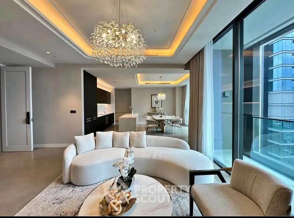 Luxurious modern living room with elegant chandelier and open kitchen layout, featuring floor-to-ceiling windows.
